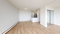 Located on the sixth floor at 5815 Yew Street in Vancouver's desirable Kerrisdale neighbourhood, this efficiently designed studio unit offers a clean, modern aesthetic throughout. The open-plan living area is bathed in natural light, courtesy of expansive floor-to-ceiling corner windows that wrap around the space and provide direct access to a private balcony. From this elevated vantage point, views of the surrounding cityscape, lush treetops, and distant mountains create a compelling backdrop. Light-toned laminate wood flooring runs continuously underfoot, lending warmth and cohesion to the interior, while crisp white walls and smooth ceilings keep the atmosphere fresh and airy. Baseboard heating lines the perimeter, ensuring year-round comfort. The kitchen is thoughtfully integrated into the layout, featuring white cabinetry, a peninsula island, stainless steel appliances, and a tile backsplash — all designed to maximize functionality within the compact footprint. The bathroom is finished with neutral stone-look tile flooring, white subway tile surrounds at the tub, a sleek vanity with a white countertop, and dark-toned cabinetry accents that add a touch of contrast. Overall, the unit presents a bright, well-appointed living environment with a clean, contemporary character suited to efficient urban living.