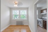 This single-floor unit offers a well-organized layout with consistent design elements throughout. Gleaming hardwood floors extend across the living areas and bedrooms, complemented by neutral-toned walls that create a clean, understated aesthetic. Ceiling fans are present in multiple rooms, enhancing airflow and comfort.

The living area features a warm accent wall and direct access to the entry door, establishing a welcoming focal point upon arrival. Multiple generously proportioned rooms offer flexible use of space, each equipped with windows fitted with horizontal blinds that allow for controlled natural light. Several rooms feature classic cast-iron radiators, indicative of a traditional heating system. Views from the windows include surrounding greenery and neighboring structures, providing a pleasant outdoor connection.

The kitchen is outfitted with dark espresso-toned cabinetry, granite-style countertops, a stainless steel sink, a white gas range, and a Whirlpool refrigerator. The tile flooring in the kitchen provides a practical transition from the hardwood in the adjoining areas.

The bathroom includes a full tub and shower combination, white tile wainscoting, a pedestal-style vanity, and a window for natural ventilation. The overall layout is functional and cohesive, making efficient use of the available space.