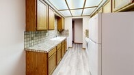 This single-floor residence offers a practical and comfortable layout across several well-defined living spaces. The galley-style kitchen is a functional highlight, featuring warm oak cabinetry, tile countertops with a built-in sink, a tile backsplash, and white appliances including a range and refrigerator. A distinctive grid-panel skylight ceiling provides bright, diffused illumination throughout the kitchen, complemented by light luxury vinyl plank flooring.

Adjacent to the kitchen, the living area is finished with plush carpet and includes a ceiling fan with light fixture. A sliding glass door opens to a private balcony with views of surrounding greenery, allowing natural light to fill the room. The neutral-toned walls throughout the residence create a clean, open atmosphere.

The bedrooms are carpeted and maintain the same neutral palette, each with warm wood-toned trim and doors. One bedroom features a window with blinds and a ceiling fan, while another includes a walk-in closet equipped with built-in shelving and a hanging rod, directly connected to a full bathroom with wood cabinetry vanity. Consistent wood baseboard trim ties the interior together, lending a cohesive, traditional aesthetic throughout the space.