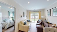 Located at 588 Bicycle Path in Port Jefferson Station, New York, this well-appointed single-floor home offers a thoughtfully designed layout that balances comfort and functionality. The living area features light hardwood flooring, recessed lighting, elegant crown molding, and large sliding glass doors that flood the space with natural light and provide direct views of the outdoor greenery. Wall sconces and tasteful coastal-inspired décor add warmth to the bright, neutral palette throughout.

The open layout connects the living and dining areas seamlessly, creating an inviting space for both relaxing and entertaining. The kitchen is outfitted with white shaker-style cabinetry, light quartz countertops, stainless steel appliances including an electric range and over-the-range microwave, and a stylish tile backsplash with a linear mosaic pattern.

The bedroom is generously proportioned, featuring large windows with outdoor views, wood-look flooring, and access to a walk-in closet. A bright, all-white bathroom offers a tub-shower combination, a single vanity with a mirror, and tile flooring. A well-lit hallway with louvered closet doors and paneled white interior doors connects the rooms, contributing to the home's clean, cohesive aesthetic.