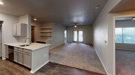 This single-floor residence offers a thoughtfully designed layout that balances modern finishes with comfortable, functional living spaces. The kitchen is a standout feature, equipped with granite-speckled quartz countertops, gray shaker-style cabinetry, stainless steel appliances including a refrigerator, electric range, and microwave, as well as a deep undermount sink. A peninsula counter opens toward the living area, creating a seamless flow between the kitchen and the main living space. The living area is generously sized, featuring plush carpet, a ceiling fan, open shelving, and glass French doors that invite natural light and provide access to the outdoors. The bedrooms are carpeted and well-proportioned, each offering ceiling fans and access to walk-in closets with built-in shelving for ample storage. The bathrooms are finished with the same quartz countertops found in the kitchen, paired with gray vanity cabinetry, vessel-style sinks, framed mirrors, and wood-look flooring. One bathroom features a full tub-shower combination with tiled surround. The consistent use of neutral gray tones, wood-look hard flooring in wet areas, and soft carpet in living and sleeping spaces gives the entire residence a cohesive, contemporary aesthetic.