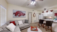 Located at 1349 N Merion Way in Fayetteville, Arkansas, this single-story, two-bedroom, one-bathroom unit offers a well-organized floor plan that maximizes every inch of its compact footprint. The open-concept living area greets you at the entrance, featuring vaulted ceilings, a ceiling fan, and a window that allows natural light to brighten the carpeted space. This area flows seamlessly into the kitchen, creating an ideal layout for daily living and entertaining.

The kitchen is equipped with white cabinetry, dark granite-style countertops, a full suite of white appliances including a refrigerator, range, microwave, and dishwasher, and a breakfast bar with seating. Wood-style flooring and an overhead ceiling fan complete the functional and clean aesthetic of this space.

Both bedrooms feature plush carpet, ceiling fans, and windows fitted with horizontal blinds. The primary bedroom comfortably accommodates a full-sized bed and dresser, while the second bedroom offers additional flexibility as a sleeping or workspace.

The shared bathroom includes a tub and shower combination with sliding glass doors and wood-style flooring. A dedicated in-unit laundry area with shelving provides added convenience. Throughout the unit, neutral wall tones create a bright and cohesive ambiance.