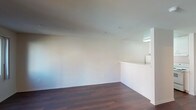 Located at 900 F Street in the heart of downtown San Diego, unit #320 is a single-floor residence featuring a clean, neutral design throughout. Dark hardwood-style flooring runs continuously across the living areas, creating a warm contrast against the bright white walls and light-toned ceilings. The open living area is well-proportioned, receiving natural light through windows and a glass-paneled exterior door that also provides access to a balcony-style entry. A ceiling fan with lighting is centrally positioned in the main living space, contributing both function and subtle style. A half-wall partition separates the kitchen from the living area, maintaining an open feel while defining the space. The galley-style kitchen is efficiently laid out with white cabinetry extending to the ceiling, white appliances including a range and refrigerator, and a built-in sink with ample counter space. The bathroom features a single-sink vanity with a light stone-toned countertop, white cabinetry below, a framed mirror with overhead vanity lighting, and a full toilet. The overall aesthetic is clean and minimal, with a consistent neutral palette that lends itself well to personalization.