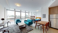 Located at 8155 Van Nuys Blvd in Panorama City, CA, this single-floor unit offers a thoughtfully designed open-concept layout that seamlessly connects the living, sleeping, and dining areas. Expansive floor-to-ceiling windows line the living space, flooding the interior with abundant natural light and offering broad views of the surrounding neighborhood. Polished concrete flooring runs throughout, lending an industrial-modern character to the space.

The living area is anchored by a comfortable seating arrangement and a plush area rug, creating a warm and inviting atmosphere. A freestanding open bookshelf serves as a stylish room divider, subtly delineating the sleeping area, which features a full-sized bed with warm wood furnishings and direct access to the oversized windows. Exposed ductwork along the ceiling adds an urban loft aesthetic.

The kitchen is well-appointed with light wood cabinetry extending to the ceiling, stainless steel appliances including a refrigerator, gas range, and microwave, and recessed lighting overhead. A dining area sits adjacent, providing a practical space for meals.

The bathroom is clean and modern, featuring a soaking tub with a combination shower enclosed by a glass panel, and fully tiled subway walls in crisp white. This unit combines contemporary design with functional living in a light-filled, open environment.