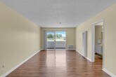 Located at 9651 Graham Street in Cypress, CA, this one-bedroom, one-bathroom unit offers a practical and well-organized single-floor layout. The open living area is finished with durable wood-style flooring that runs throughout the main living spaces, complemented by neutral-toned walls and a textured ceiling. A ceiling fan with integrated lighting adds both comfort and functionality, while a sliding glass door floods the room with natural light and provides access to an outdoor area with views of surrounding greenery. The galley-style kitchen is efficiently designed with white shaker cabinetry, granite-look countertops, a stainless steel double sink, and black appliances including a gas range, microwave, and refrigerator — all set atop wood-style flooring for a cohesive look. The spacious primary bedroom features plush wall-to-wall carpeting, a large window that invites natural light and outdoor views, and access to a closet. The bathroom is cleanly appointed with a tub-shower combination, a vanity featuring a granite-look countertop, and matching wood-style flooring. A connecting hallway ties the rooms together, making for a functional and comfortable living space.
