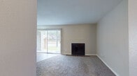 This single-floor residence offers a straightforward and functional layout designed for comfortable everyday living. The living room serves as the focal point of the home, featuring a classic fireplace with a tile surround and a large sliding glass door fitted with vertical blinds that opens to an outdoor patio area. Natural light fills the space, which transitions between hardwood-style flooring near the entry and plush carpeting throughout the main living area. The neutral, warm-toned walls and clean white ceilings create a bright and inviting ambiance throughout.

The galley-style kitchen is efficiently arranged with light-toned cabinetry, speckled countertops, a dishwasher, and a full-size refrigerator, all set atop hardwood-style flooring. A door in the kitchen provides additional access to the exterior.

The bedrooms are generously sized, each finished with soft carpeting and neutral walls that offer a calm, restful environment. One bedroom features built-in shelving, adding practical storage. The bathroom is clean and well-appointed, complete with a tiled shower-tub combination, a vanity with speckled countertops, and hardwood-style flooring. Overall, the space maintains a simple, move-in-ready character with consistent finishes throughout.