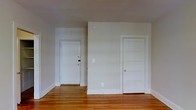 This single-floor space presents a straightforward and functional layout distinguished by its warm hardwood flooring, which runs throughout the room and adds a natural, inviting character. The walls are finished in a clean, neutral tone that reflects light evenly and contributes to a bright, open atmosphere. Two white panel doors are visible — one appearing to serve as an entry point and the other leading to an adjoining room or closet — providing practical connectivity within the space. The white door frames and baseboards offer a classic contrast against the wood floors, lending a timeless quality to the interior. A standard wall plate and outlet are positioned on the main wall, suggesting a ready-to-use, move-in-ready condition. The ceiling is smooth and unadorned, maintaining a clean, minimalist aesthetic throughout. Overall, the space feels airy and uncluttered, making it highly adaptable for a variety of uses. The combination of hardwood floors, neutral finishes, and simple architectural details creates a cohesive and practical environment suited to a range of furnishing styles and functional arrangements.
