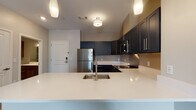 Located at 42 Wellman Street in Lowell, Massachusetts, this single-floor residence offers a well-designed layout with modern finishes throughout. The open-concept living and dining area is bright and spacious, featuring wood-style flooring, neutral-toned walls, and large windows dressed with vertical blinds that allow ample natural light to fill the space. Pendant and flush-mount lighting add a contemporary touch to the interior.

The kitchen is a standout feature, outfitted with deep navy shaker-style cabinetry, crisp white quartz countertops, a stainless steel undermount sink, and a full suite of stainless steel appliances including a refrigerator, range, microwave, and dishwasher. A kitchen island with an extended breakfast bar provides additional workspace and a natural connection to the living area.

The bathroom is finished with warm wood-toned cabinetry, a white vanity countertop, a wall-mounted storage cabinet, and light wood-look tile flooring, creating a clean and functional space. The unit also includes a dedicated utility room housing a stacked GE washer and dryer unit alongside a water heater, offering convenient in-unit laundry. The overall design balances practicality with contemporary style, making this a well-appointed residence in Lowell.