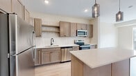 Located at 6701 W 78th St in Bloomington, MN, this two-bedroom, two-bathroom residence offers a well-designed single-level layout with a thoughtful mix of hard-surface and carpeted flooring. The open-concept kitchen and living area serves as the heart of the home, featuring light wood cabinetry, stainless steel appliances including a refrigerator, range, microwave, and dishwasher, a tiled backsplash, and a central island with a white countertop and pendant lighting above. Light hardwood-style flooring flows throughout the main living area, which opens to a private balcony through sliding glass doors, offering outdoor views of the surrounding community. Both bedrooms are carpeted and filled with natural light from large windows. The primary bedroom is generously sized and includes a dedicated closet with built-in shelving. The primary bathroom features a dual-sink vanity with white countertops, matte black fixtures, a large framed mirror, and wood-look flooring. The second bathroom includes a full tub-shower combo with a curved rod and matte black hardware. A dedicated laundry area houses a stacked full-size washer and dryer unit alongside additional shelving for storage. Two closets provide ample organizational space throughout the residence.