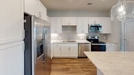 This single-floor residence in Greensboro, NC offers a thoughtfully designed open-concept layout that seamlessly connects the kitchen and living areas. The kitchen is a standout feature, showcasing white shaker cabinetry, granite countertops, a subway tile backsplash, and a full suite of stainless steel appliances, including a French door refrigerator, electric range, built-in microwave, and dishwasher. A center island with pendant lighting adds both workspace and visual appeal. Rich wood-look flooring flows throughout the main living areas, while a ceiling fan and French doors leading to a balcony enhance the bright, airy living room.

The bedrooms are finished with plush carpet, ceiling fans, and window blinds that allow natural light. A spacious walk-in closet with wire shelving provides generous storage. The bathrooms are well-appointed, featuring white vanities with stone-topped counters and tile flooring. One bathroom includes a soaking tub, while another offers a walk-in shower. Neutral gray walls and clean white trim throughout lend the space a modern, cohesive aesthetic.