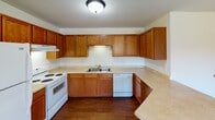 Located at 721 S Victory Dr in Mankato, Minnesota, this single-floor unit offers a practical and comfortable layout designed for everyday living. The kitchen is a standout feature, showcasing rich oak cabinetry with ample upper and lower storage, light-toned countertops in a U-shaped configuration, hardwood flooring, and white appliances including a range, dishwasher, and a double-basin sink. The space flows naturally into the living area, which is finished with neutral carpet, crisp white walls, warm wood baseboards and trim, and a window that invites natural light. The bedrooms continue the carpeted aesthetic, each featuring wood-trimmed windows with views of the surrounding area and bi-fold closet doors with warm wood paneling for generous storage. The bathroom is well-appointed with a wood-cabinet vanity, white countertop, a framed mirror with globe lighting above, and hardwood flooring that carries through from the adjacent hallway. Throughout the unit, consistent wood accents—from door frames to trim—create a cohesive, warm tone. The textured ceilings and neutral color palette provide a clean, move-in-ready canvas adaptable to a variety of styles.