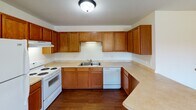 Located at 721 S Victory Dr in Mankato, Minnesota, this single-floor unit offers a practical and comfortable layout designed for everyday living. The kitchen is a standout feature, showcasing rich oak cabinetry with ample upper and lower storage, light-toned countertops in a U-shaped configuration, hardwood flooring, and white appliances including a range, dishwasher, and a double-basin sink. The space flows naturally into the living area, which is finished with neutral carpet, crisp white walls, warm wood baseboards and trim, and a window that invites natural light. The bedrooms continue the carpeted aesthetic, each featuring wood-trimmed windows with views of the surrounding area and bi-fold closet doors with warm wood paneling for generous storage. The bathroom is well-appointed with a wood-cabinet vanity, white countertop, a framed mirror with globe lighting above, and hardwood flooring that carries through from the adjacent hallway. Throughout the unit, consistent wood accents—from door frames to trim—create a cohesive, warm tone. The textured ceilings and neutral color palette provide a clean, move-in-ready canvas adaptable to a variety of styles.