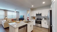 This single-floor residence showcases a thoughtfully designed open-concept layout with consistent wood-look flooring that flows seamlessly throughout the space. The kitchen serves as a central highlight, featuring crisp white shaker cabinetry, granite countertops, and a full suite of stainless steel appliances including a French door refrigerator, range, microwave, and dishwasher. A kitchen island with an undermount sink provides additional workspace and casual seating, while recessed lighting illuminates the area effectively.

The entryway opens directly into the kitchen and living area, creating an immediate sense of openness. The living area benefits from multiple windows dressed with horizontal blinds and sheer curtains, allowing ample natural light to brighten the neutral-toned interior. A ceiling fan adds both function and comfort to this space.

The bedroom is a well-proportioned retreat, featuring a ceiling fan, a large window for natural light, and access to a walk-in closet. The bathroom is finished with granite-topped white vanity cabinetry, a large mirror with overhead lighting, and a tiled tub-shower combination featuring marble-look tile. The consistent use of neutral tones, granite surfaces, and white cabinetry throughout creates a cohesive, modern aesthetic across the entire residence.