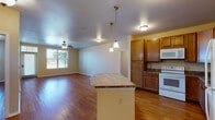 This single-story residence is thoughtfully designed with an open-concept layout that connects the kitchen and living areas, creating a cohesive and functional flow throughout the space. Warm hardwood-style flooring extends consistently across the main living areas, contributing to a clean and inviting aesthetic.

The kitchen serves as a central feature, equipped with medium-toned wood cabinetry offering ample storage, granite-style countertops, and a full suite of white appliances including a range, microwave, dishwasher, and refrigerator. A curved peninsula island with matching countertop provides additional workspace and is illuminated by pendant lighting overhead, enhancing both function and visual appeal.

The living area is generously proportioned, featuring a ceiling fan with light fixture and windows with outdoor views that bring in natural light. A dedicated bedroom offers hardwood-style flooring, a ceiling fan, and a window with exterior views. A spacious walk-in closet provides organized wire shelving for storage.

The bathroom features tile flooring, a wood-vanity with granite-style countertop, and an accessible shower with grab bars. A dedicated laundry area accommodates a full-size washer and dryer, adding everyday convenience to the space.