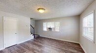 Located at 1601 Gray Pl in Baltimore, MD, this two-floor home offers a well-organized layout with updated finishes and a neutral color palette throughout. The main level features durable wood-style flooring that flows through the living and dining areas, complemented by textured ceilings and a front entry door with accent glass panels that invite natural light into the space. Multiple windows fitted with blinds brighten the main living area, which also includes a staircase with a black metal railing leading to the upper floor.

The kitchen is thoughtfully appointed with gray shaker-style cabinetry, white countertops, and a full suite of white appliances including a gas range, dishwasher, and refrigerator. A skylight-style overhead fixture provides ample illumination. Adjacent to the kitchen, a dining or utility area features additional built-in cabinetry and a back door flanked by windows overlooking the surrounding neighborhood.

The bathroom is clean and bright, featuring a tiled tub-and-shower combination, a window for ventilation, and wood-style flooring. The upper-level bedrooms are carpeted and well-lit, each equipped with windows that allow natural light and views of the neighborhood. The overall ambiance throughout the home is clean, functional, and move-in ready.