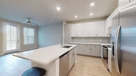 Located at 4902 Cosmos Circle in Wimauma, FL, this single-story home offers a thoughtfully designed layout with one bedroom, three bathrooms, and a dedicated closet. The open-concept kitchen serves as the centerpiece of the living area, showcasing crisp white upper cabinetry, light gray lower cabinets, a classic subway tile backsplash, and gleaming white quartz countertops. A central island with a built-in sink and dishwasher provides additional prep space and casual seating. Stainless steel appliances — including a range, over-the-range microwave, and French door refrigerator — complete the modern culinary space. Light wood-style flooring flows seamlessly throughout the home, complemented by neutral wall tones and recessed lighting. The bedroom is generously sized, featuring a ceiling fan, natural light from a window, and direct access to a private en-suite bathroom. The walk-in closet is equipped with multi-tiered wire shelving for organized storage. The bathrooms are finished with white quartz vanities, sleek cabinetry, and one features a frameless glass-enclosed walk-in shower with white subway tile surround. The overall aesthetic is clean, contemporary, and move-in ready.