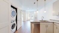 Located at 1866 E 93rd St in Cleveland, Ohio, this single-floor unit offers a clean, modern design with a bright and open layout throughout. Light hardwood-style flooring flows continuously across the entire space, complementing the crisp white walls and creating a cohesive, contemporary aesthetic.

The kitchen is a standout feature, outfitted with a full suite of stainless steel appliances, including a refrigerator, electric range, over-the-range microwave, and dishwasher. White cabinetry with sleek brushed hardware extends to the ceiling for ample storage, while granite countertops add a polished finish. Pendant lighting above the kitchen island provides both functional illumination and a stylish focal point.

The open living area benefits from generous natural light streaming through large windows with views of the surrounding neighborhood. Recessed lighting supplements natural light throughout, ensuring the space remains bright at all times. The living area offers a flexible, open canvas well-suited for a variety of furniture arrangements.

A dedicated in-unit laundry area houses a stacked washer and dryer, adding everyday convenience. The unit also features a spacious secondary room with neutral tones, recessed lighting, and ample wall space. Overall, the unit presents a well-appointed, move-in-ready living environment with modern finishes throughout.