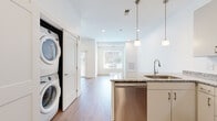 Located at 1866 E 93rd St in Cleveland, Ohio, this single-floor unit offers a clean, modern design with a bright and open layout throughout. Light hardwood-style flooring flows continuously across the entire space, complementing the crisp white walls and creating a cohesive, contemporary aesthetic.

The kitchen is a standout feature, outfitted with a full suite of stainless steel appliances, including a refrigerator, electric range, over-the-range microwave, and dishwasher. White cabinetry with sleek brushed hardware extends to the ceiling for ample storage, while granite countertops add a polished finish. Pendant lighting above the kitchen island provides both functional illumination and a stylish focal point.

The open living area benefits from generous natural light streaming through large windows with views of the surrounding neighborhood. Recessed lighting supplements natural light throughout, ensuring the space remains bright at all times. The living area offers a flexible, open canvas well-suited for a variety of furniture arrangements.

A dedicated in-unit laundry area houses a stacked washer and dryer, adding everyday convenience. The unit also features a spacious secondary room with neutral tones, recessed lighting, and ample wall space. Overall, the unit presents a well-appointed, move-in-ready living environment with modern finishes throughout.