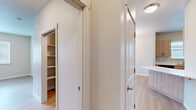This single-floor unit is designed with a clean, contemporary aesthetic throughout, featuring light wood-style flooring and neutral warm-toned walls that create a cohesive and inviting atmosphere. The kitchen is efficiently laid out with light wood cabinetry, white countertops, and black appliances including a refrigerator, electric range, and microwave, providing ample storage and counter space for everyday use.

The living area is bright and open, benefiting from multiple windows fitted with horizontal blinds that allow natural light to filter in. A ceiling fan overhead adds both function and comfort to the space. A door leads to an outdoor area, further enhancing the connection to natural light.

The bedrooms are well-proportioned with the same light wood flooring and neutral walls. Windows provide views of the surrounding neighborhood. One bedroom includes access to a walk-in closet with built-in shelving, offering generous storage. An additional door off the hallway provides further storage or utility access.

The bathroom features patterned tile flooring, a wood-toned vanity with a white countertop, a large mirror, and a brushed nickel towel bar, giving the space a polished, modern finish.
