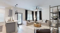 This single-story space showcases a clean, contemporary design characterized by crisp white walls, light wood-tone flooring, and a cohesive neutral palette carried throughout every room. The open-concept layout connects the kitchen and living area seamlessly, creating a spacious and functional flow. The kitchen is a standout feature, equipped with gray shaker-style cabinetry, white quartz countertops, stainless steel appliances including a refrigerator, range, and microwave, and a central island with an undermount sink. A built-in wine rack adds a refined touch, while a pair of sleek black pendant lights anchor the space with modern style. The living area benefits from natural light through large windows dressed with blinds, and a ceiling fan with integrated lighting enhances comfort. The bedrooms are well-proportioned, each featuring light flooring, ceiling fans, and generous windows that invite natural light. The bathroom is finished with gray cabinetry, a white vanity, and a framed mirror with black hardware accents. A dedicated laundry room accommodates a full-size washer and dryer side by side. Throughout the space, consistent use of black hardware and dark-paneled interior doors provides a polished, unified aesthetic.