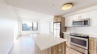 Located in the heart of downtown Stamford, CT, this thoughtfully designed 2-bedroom, 3-bathroom residence offers a clean, contemporary aesthetic throughout. The open-concept kitchen and living area forms the centerpiece of the home, featuring light wood-style flooring, crisp white walls, and abundant natural light streaming through large windows that frame sweeping city views. The kitchen is well-appointed with stainless steel appliances — including a range, microwave, and dishwasher — paired with two-tone cabinetry combining white upper cabinets and warm wood-grain lower cabinets, white quartz countertops, a subway tile backsplash, and a central island that doubles as a breakfast bar. The living area flows seamlessly from the kitchen, bathed in sunlight with direct city views. Both bedrooms are generously proportioned, carpeted for comfort, and feature large windows that showcase the Stamford skyline. The spacious primary bedroom includes a full sliding-door closet. The three bathrooms maintain a consistent modern design with white subway tile tub surrounds, wood-accented vanities, brushed nickel fixtures, and neutral tile flooring. The overall ambiance is bright, clean, and contemporary — ideal for urban living in one of Connecticut's most vibrant cities.