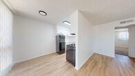 This single-floor unit is designed with a clean, functional layout that maximizes its available space. The living area is bright and open, featuring light wood laminate flooring and large windows fitted with vertical blinds that allow generous natural light to filter in. A ceiling fan with an integrated light fixture adds both comfort and practicality to this space.

The kitchen is efficiently arranged and features white cabinetry with matte black hardware, white countertops, a single-basin sink with a matte black faucet, and a gas range with an overhead exhaust hood. A stainless steel refrigerator completes the appliance package. The kitchen is partially separated from the living area by a partial wall, creating a defined yet connected cooking space. Light wood flooring continues throughout the kitchen.

The bedrooms are carpeted in a neutral beige tone, offering a softer underfoot feel. Each room includes a window with vertical blinds, providing natural light and a sense of openness. The walls throughout are painted crisp white, contributing to the unit's clean and airy ambiance.

The bathroom is finished in a simple, functional style with white tile surrounding a full soaking tub and shower combination, light wood flooring, a white toilet, and matte black hardware accents. Textured ceilings are present throughout the unit.