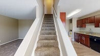 Located at 1112 Ashberry Village Dr in Columbus, Ohio, this two-story home offers a practical and comfortable layout across two evenly divided floors. The main level houses the living room and kitchen, while the upper floor is dedicated to the bedrooms and bathroom. The living room features neutral-toned walls, plush carpet, a window with natural light, a wall-mounted air conditioning unit, and a baseboard heater. The kitchen is well-appointed with rich, warm-toned wood cabinetry, granite-look countertops, hardwood-style flooring, a double sink, and black appliances including a range and refrigerator. Both bedrooms are carpeted and finished in soft neutral tones, each featuring ceiling fans, windows with blinds for natural light, and closet access. The primary bedroom offers a generous footprint with a dedicated closet. The bathroom includes a full tub and shower combination with brushed nickel fixtures. A hallway connects the upper-level spaces, and a dedicated closet provides additional storage. The home also features an outdoor patio area, visible from the Matterport model, adding outdoor functionality to the property.