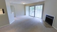 Located at 650 Lake Front Dr in Raleigh, North Carolina, this single-floor residence offers a clean, functional layout designed for comfortable everyday living. The main living area is generously sized, finished with wall-to-wall carpeting that adds warmth underfoot. Neutral-toned walls throughout provide a versatile backdrop suited to a variety of interior styles. A standout feature of the living space is the full-width sliding glass door dressed with vertical blinds, which floods the room with natural light and provides direct access to an outdoor balcony. The balcony overlooks a lush, tree-lined setting, offering a serene and private outdoor retreat. The transition between the carpeted living area and the tiled entryway zone is clearly defined, adding a practical touch to the floor plan. Flush ceiling lighting provides consistent illumination throughout. The overall ambiance of the space is bright, open, and tranquil, with the greenery visible through the large glass door contributing to a connection with the natural surroundings. The single-level layout ensures easy accessibility and a seamless flow throughout the home.
