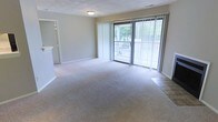 Located at 650 Lake Front Dr in Raleigh, North Carolina, this single-floor residence offers a clean, functional layout designed for comfortable everyday living. The main living area is generously sized, finished with wall-to-wall carpeting that adds warmth underfoot. Neutral-toned walls throughout provide a versatile backdrop suited to a variety of interior styles. A standout feature of the living space is the full-width sliding glass door dressed with vertical blinds, which floods the room with natural light and provides direct access to an outdoor balcony. The balcony overlooks a lush, tree-lined setting, offering a serene and private outdoor retreat. The transition between the carpeted living area and the tiled entryway zone is clearly defined, adding a practical touch to the floor plan. Flush ceiling lighting provides consistent illumination throughout. The overall ambiance of the space is bright, open, and tranquil, with the greenery visible through the large glass door contributing to a connection with the natural surroundings. The single-level layout ensures easy accessibility and a seamless flow throughout the home.
