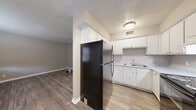 This 2-bedroom, 1-bathroom unit offers a practical and well-organized single-floor layout. Throughout the space, wood-look laminate flooring in a warm, medium-toned finish provides a cohesive aesthetic, complemented by neutral gray walls and white baseboards. Textured ceilings are present throughout.

The kitchen is efficiently designed in an L-shaped configuration, featuring white cabinetry with ample upper and lower storage, a double-basin sink, a black electric range, and a full-size refrigerator. The layout opens toward the living area, enhancing the sense of connectivity between spaces.

The living room offers an open, adaptable area with multiple outlets and ventilation registers, connected via a hallway to the rest of the unit. Both bedrooms are well-proportioned, with the primary bedroom offering a comfortable footprint. Each bedroom includes windows with blinds that allow natural light, and at least one bedroom features a built-in closet with a hanging rod for added storage convenience.

The bathroom includes a single-sink vanity with a speckled countertop, a large mirror, a toilet, and a tub-shower combination with white surround. The unit also includes a dedicated closet for additional storage needs, rounding out a straightforward and functional floor plan.