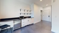 Located at 622-626 Third Ave S in Nashville, TN, this efficiently designed one-bedroom, one-bathroom unit delivers a modern, minimalist aesthetic across a single floor. The open layout maximizes every square foot, with polished concrete-style flooring running throughout, lending a sleek, contemporary feel to the space.

The living and kitchen area features a well-appointed kitchenette outfitted with white cabinetry, dark countertops, stainless steel appliances including a compact refrigerator and microwave, and an integrated sink. Open wall-mounted shelving with matte black brackets adds both storage and visual interest, keeping the space functional without feeling cluttered. A large window allows generous natural light to pour in, illuminating the crisp white walls and providing views of the surrounding Nashville streetscape.

The bedroom is a spacious retreat relative to the overall footprint, finished with the same cool-toned grey walls and durable flooring, creating a calm and restful environment. A full-length mirror and under-bed storage contribute to the room's practicality.

The bathroom is cleanly finished with large-format tile flooring, bright white walls, and matte black hardware accents, maintaining the unit's consistent modern design language. Accessibility grab bars are thoughtfully integrated throughout.