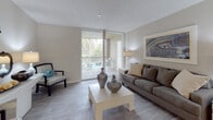 This single-floor residence at 1857 Coral Ridge Drive in Coral Springs, Florida, offers a well-designed layout across two bedrooms and two bathrooms. The living area features wood-style flooring, a textured ceiling, and floor-to-ceiling vertical blinds that frame sliding glass doors leading to a private balcony. The outdoor space overlooks mature tropical greenery, allowing natural light to fill the room throughout the day.

The kitchen is equipped with dark espresso cabinetry, stainless steel appliances including a microwave and refrigerator, a gas range, and light stone countertops. A peninsula with a breakfast bar separates the kitchen from the adjacent dining area, creating a practical open-concept flow.

Both bedrooms are generously proportioned with plush carpeting, large windows that invite natural light, and ceiling fans for comfort. The primary bedroom connects to an en-suite bathroom through an elegant arched entryway, featuring dark vanity cabinetry, a wide mirror with lighted fixtures, and tile flooring. A mirrored sliding-door closet with built-in shelving provides ample storage. The second bathroom mirrors the same refined design, maintaining a consistent aesthetic throughout the residence.