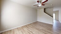 This two-story home offers a thoughtfully designed layout spread across two well-proportioned floors. The main level features a bright and open living room with light wood-look flooring and a ceiling fan, a dedicated dining area with a modern multi-light chandelier, and a kitchen equipped with dark espresso cabinetry, granite-style countertops, subway tile backsplash, and stainless steel Whirlpool appliances including a side-by-side refrigerator and electric range. A half or full bathroom on the main level adds convenience, and the open staircase connects seamlessly to the upper floor. Upstairs, the generous primary bedroom benefits from multiple windows that invite natural light, complemented by plush carpeting. It is accompanied by a spacious walk-in closet outfitted with wire shelving systems providing ample storage. The primary bathroom features wood-look flooring, a dark-toned vanity with a white countertop, a large mirror, and a glass-enclosed walk-in shower. Two additional carpeted bedrooms each include double-door closets. The secondary bathrooms maintain the same clean, neutral aesthetic with hardwood-style flooring throughout. The home's consistent warm neutral palette, ceiling fans, and abundant natural light create a comfortable and cohesive living environment.