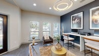 This single-floor commercial suite is designed with a refined contemporary aesthetic, combining functionality with sophisticated style. The main workspace is anchored by a sleek, elongated white desk accommodating dual workstations, set against a dramatic deep navy accent wall adorned with large-scale framed botanical artwork. Tall decorative planters with sculptural branches add organic texture to the space. Overhead, a striking dual-ring circular chandelier serves as a focal point, complementing the recessed lighting throughout.

Natural light flows generously through multiple windows fitted with white plantation shutters, offering views of the surrounding greenery. The seating area features a plush upholstered armchair, layered area rugs over large-format tile flooring, and curated gold accent tables that elevate the overall aesthetic.

A private conference room, accessible through a frosted-glass interior door framed with sheer draping, provides a more intimate setting with a round table and upholstered chairs — ideal for meetings or consultations. The entry area features floor-to-ceiling glazing and dark-framed double doors, offering a welcoming, professional first impression with clear views to the outdoor surroundings. Throughout, the design balances warmth, modern elegance, and practical workspace functionality.