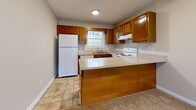 Located at 1205 5th St NE in Hickory, NC, this single-floor, two-bedroom, two-bathroom residence offers a well-organized layout designed for functional, everyday living. The open kitchen and living room combination serves as the heart of the home, with the kitchen featuring warm oak cabinetry, light countertops, a peninsula with additional storage, and white appliances including a range, refrigerator, and dishwasher. Tile-style flooring runs throughout the kitchen, while the adjoining living room is finished with plush carpeting and French doors that invite natural light and provide outdoor access. Both bedrooms are carpeted and include ceiling fans with lighting. The primary bedroom offers a comfortable footprint with natural light from a window, while the second bedroom mirrors a similar layout. Two dedicated closets provide additional storage throughout the unit. The two bathrooms are finished with tile-style flooring, warm-toned vanities with white countertops, and full tub-shower combinations with chrome fixtures. A hallway connects the rooms, contributing to a coherent and easy-to-navigate floor plan. Neutral wall tones and textured ceilings carry throughout, lending the space a clean, understated aesthetic.
