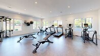 Located at 2708 Old Lebanon Pike in Nashville, TN, this fitness center offers a thoughtfully designed exercise space that accommodates a wide range of workout routines. The room is bathed in natural light, courtesy of large windows along multiple walls that provide open views of the surrounding greenery, creating an energizing atmosphere for exercise.

The space is outfitted with an impressive array of equipment. Cardio options include multiple treadmills, a rowing machine, a stationary bike, and an elliptical trainer. A multi-functional cable machine anchors one area of the room, ideal for strength and resistance training. A full rack of dumbbells is neatly organized alongside adjustable workout benches, catering to free weight exercises at various intensity levels. Wall-mounted medicine balls and a BOSU balance trainer round out the functional fitness offerings.

The interior is finished with clean white walls, recessed lighting, and durable flooring suited for high-activity use. Full-length mirrors are strategically placed to maximize the sense of space and support proper form during workouts. A wall-mounted television and a water station add convenience. The open, uncluttered layout ensures ease of movement between stations, making this fitness center a practical and well-appointed destination for residents pursuing their health and wellness goals.