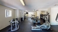 This well-equipped fitness center at 3040 E Shea Blvd in Phoenix, Arizona, offers a comprehensive workout environment spread across a single floor. The space features a dark rubber flooring throughout, providing both durability and comfort underfoot. Textured ceilings with fluorescent lighting ensure the entire area is brightly and evenly lit.

The cardio section is generously stocked with multiple treadmills, elliptical trainers, stationary bikes, and a rowing machine, offering users a wide variety of aerobic exercise options. A dedicated strength training area includes a multi-function cable machine and weight bench, catering to resistance-based workouts. Wall-mounted mirrors in select areas visually expand the space and allow exercisers to monitor their form, while a wall-mounted flat-screen television adds an entertainment element to cardio sessions.

Natural light filters into the gym through several windows, creating a pleasant atmosphere. A standout feature is the set of large glass French doors that open to an outdoor area, offering views of lush surrounding greenery and a glimpse of what appears to be a pool area beyond, seamlessly connecting the interior workout space to the outdoors. The overall ambiance is clean, functional, and well-maintained, making it a practical and inviting facility for a full-body fitness routine.