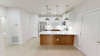 This well-designed 1-bedroom, 1-bathroom residence offers a thoughtful layout across a single floor, combining modern aesthetics with practical functionality. Light-toned luxury vinyl plank flooring flows seamlessly throughout the entire space, creating a cohesive and airy feel.

The kitchen is a standout feature, showcasing a two-tone design with crisp white shaker cabinetry paired with warm wood-toned lower cabinetry on the peninsula. A quartz countertop extends across the workspace and peninsula, complemented by a white subway tile backsplash. Three brushed nickel pendant lights hang above the peninsula, adding both style and task lighting. Stainless steel appliances — including a refrigerator, dishwasher, over-the-range microwave, and electric range — complete this well-appointed kitchen.

The bedroom is a comfortable, well-proportioned space with a ceiling fan, a window that brings in natural light, and direct access to a dedicated closet with built-in shelving. A secondary door provides convenient connectivity within the unit.

The full bathroom features white cabinetry with a long vanity, a framed mirror with overhead lighting, and a soaking tub. A notable convenience is the in-unit stacked washer and dryer, tucked neatly into a closet adjacent to the bathroom. Clean white walls and recessed lighting throughout the unit enhance the bright, modern ambiance.