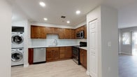 Located at 171 East St in Methuen, Massachusetts, this single-floor unit offers a well-designed layout with contemporary finishes throughout. The kitchen is a standout feature, showcasing rich warm-toned wood cabinetry, a subway tile backsplash, light countertops, and a full suite of stainless steel appliances including a dishwasher, range, and built-in microwave. A stacked washer and dryer unit is conveniently integrated into the kitchen area, providing in-unit laundry without sacrificing space. The flooring in the main living and kitchen areas consists of light-toned wood-look planks that lend a clean, modern feel to the space. The living area is open and airy, featuring neutral gray walls, recessed lighting, and a sliding glass door flanked by additional windows that invite natural light and provide access to an outdoor area. The bedroom is generously sized with plush gray carpeting, neutral walls, and a bright window overlooking the outdoors. The full bathroom is finished with light tile flooring, a wood-toned vanity with a stone-look countertop, and a full tub-shower combination. Throughout the unit, crisp white trim, consistent neutral tones, and recessed lighting contribute to a cohesive and move-in-ready atmosphere.
