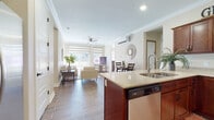 This single-floor residence offers a thoughtfully designed open-concept layout that seamlessly connects the kitchen, dining, and living areas. The kitchen is outfitted with rich dark wood cabinetry, granite countertops, stainless steel appliances including a range, microwave, and dishwasher, and a peninsula with a double sink — ideal for both cooking and entertaining. Wood-look tile flooring flows through the main living areas, adding warmth and a cohesive aesthetic throughout.

The living room is bright and welcoming, featuring large windows with layered roller shades that allow for natural light control, a ceiling fan, and a wall-mounted mini-split unit for climate comfort. The adjacent dining area provides an intimate space for meals. Crown molding throughout the main living areas adds a refined architectural touch.

The bedroom is carpeted for comfort, benefits from multiple windows with outdoor views, and includes a spacious walk-in closet with built-in shelving for generous storage. The primary bathroom features dual vessel sinks atop granite counters with dark wood cabinetry, LED-lit mirrors, and wood-look tile flooring. A second bathroom offers a single vessel sink vanity with a similarly elegant finish, completing this well-appointed residence.