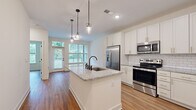 Located at 96 E Catawba St in Belmont, NC, this well-appointed one-bedroom, one-bathroom unit offers a thoughtfully designed single-floor layout that maximizes every square foot. Warm hardwood-style flooring flows throughout the entire space, creating a cohesive and inviting atmosphere.

The open-concept kitchen is a standout feature, showcasing white shaker cabinetry with gold hardware, a classic subway tile backsplash, and a granite-topped center island with a matte black sink and pendant lighting overhead. Stainless steel appliances — including a French door refrigerator, range, and microwave — complete this modern culinary space. Adjacent built-in shelving adds both function and character near the entry.

The living room is bright and airy, benefiting from large windows and a glass-paneled door that frame lush outdoor greenery and provide access to an outdoor area. The bedroom is a comfortable, light-filled retreat with a generous window offering garden views and direct access to the bathroom and closet.

The bathroom is clean and contemporary, featuring granite countertops, white cabinetry with gold hardware, a glass-enclosed walk-in shower with matte black fixtures, and continued hardwood-style flooring. The closet provides convenient in-unit storage. This unit combines modern finishes with a practical layout in a charming Belmont setting.