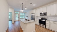 Located at 96 E Catawba St in Belmont, NC, this well-appointed one-bedroom, one-bathroom unit offers a thoughtfully designed single-floor layout that maximizes every square foot. Warm hardwood-style flooring flows throughout the entire space, creating a cohesive and inviting atmosphere.

The open-concept kitchen is a standout feature, showcasing white shaker cabinetry with gold hardware, a classic subway tile backsplash, and a granite-topped center island with a matte black sink and pendant lighting overhead. Stainless steel appliances — including a French door refrigerator, range, and microwave — complete this modern culinary space. Adjacent built-in shelving adds both function and character near the entry.

The living room is bright and airy, benefiting from large windows and a glass-paneled door that frame lush outdoor greenery and provide access to an outdoor area. The bedroom is a comfortable, light-filled retreat with a generous window offering garden views and direct access to the bathroom and closet.

The bathroom is clean and contemporary, featuring granite countertops, white cabinetry with gold hardware, a glass-enclosed walk-in shower with matte black fixtures, and continued hardwood-style flooring. The closet provides convenient in-unit storage. This unit combines modern finishes with a practical layout in a charming Belmont setting.