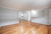 Located at 645 Belle Terre Rd in Port Jefferson, NY, this single-floor space offers a clean, functional layout with consistent design throughout. Gleaming hardwood floors run across the living areas and bedrooms, reflecting natural light and lending warmth to the neutral gray-painted walls accented by crisp crown molding. The open living area is generously proportioned, featuring a pass-through counter that connects to the kitchen and provides views into the adjoining rooms, creating a cohesive flow throughout the space. The galley-style kitchen is well-appointed with white cabinetry, granite countertops, a stainless sink, and white appliances including a range and refrigerator, all complemented by light wood-style flooring. The bedrooms continue the hardwood floor theme and are finished with crown molding; window-mounted air conditioning units and baseboard heating ensure year-round comfort, while windows frame views of the surrounding greenery. The bathroom is finished in bright white marble-style tile that extends from floor to ceiling in the tub/shower surround, paired with neutral tile flooring for a clean, polished look. Overall, the space presents a well-maintained, move-in-ready environment with classic finishes and a practical layout suited for everyday living.