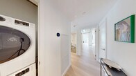 Located on the 16th floor at 748 Bathurst Street in Toronto's vibrant Annex neighbourhood, this two-bedroom, one-bathroom residence blends industrial-modern design with refined finishes. The open-concept living and dining area is defined by striking exposed concrete ceilings with visible structural columns and pipework, contrasted by crisp white walls and light hardwood flooring that run throughout. Large floor-to-ceiling windows flood the space with natural light and frame panoramic views of the Toronto skyline and city streets below. The kitchen is outfitted with contemporary cabinetry in a warm wood tone, a sleek double stainless steel sink, and white countertops, positioned to take full advantage of the sweeping urban vistas. The primary bedroom continues the exposed concrete aesthetic and benefits from generous windows with broad cityscape views, complemented by ample closet space. The second bedroom is equally well-lit, sharing the same elevated outlook. A clean, bright hallway connects the rooms and includes a convenient in-unit stacked washer and dryer. The bathroom is finished in all-white tile with a soaking tub and modern chrome fixtures, maintaining the unit's cohesive, contemporary palette throughout.