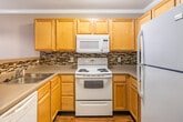 Located at Grand Summit in Greensboro, NC, this one-bedroom, one-bathroom residence offers a thoughtfully designed single-level layout that makes efficient use of its space. The combined kitchen and living area serves as the heart of the unit, where the kitchen features light maple cabinetry, light-toned countertops, white appliances including a refrigerator, electric range, dishwasher, and built-in microwave, all set on rich hardwood-style flooring. A skylight brightens the kitchen, while a pass-through opening connects it to the carpeted living area, which is equipped with a ceiling fan and light fixture. Large windows in the living space invite abundant natural light and offer views of surrounding greenery.

The spacious primary bedroom is generously sized, finished with soft carpet, a ceiling fan, and a large multi-pane window that frames outdoor tree views. Two closets provide ample storage throughout the unit. The full bathroom continues the hardwood-style flooring and includes a tub/shower combination, toilet, and towel bars. Neutral warm tones throughout create a cohesive, calm ambiance well-suited for comfortable everyday living.