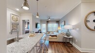 This thoughtfully designed single-floor residence blends modern elegance with comfortable living across a well-planned open layout. Rich hardwood flooring flows throughout, anchoring each room with warmth and continuity.

The kitchen is a standout feature, outfitted with crisp white shaker cabinetry, granite countertops, a marble-tiled backsplash, stainless steel appliances, and under-cabinet lighting. A granite-topped peninsula with seating provides an ideal space for casual dining, illuminated by stylish pendant lights overhead. A built-in wine rack adds a refined touch.

The open-concept living area is bright and inviting, with crown molding, a ceiling fan, and large windows that fill the space with natural light. The dining nook offers a cozy retreat with built-in shelving and space for an intimate table setting.

The primary bedroom is a serene escape, featuring a generous window with outdoor views, crown molding, and an en-suite bathroom with a dual-sink granite vanity, white cabinetry, and access to a walk-in closet. A second well-proportioned bedroom benefits from its own ceiling fan and natural light. The guest bathroom mirrors the same refined finishes, with a granite-topped white vanity and framed mirror. Every detail reflects a consistent commitment to quality and style throughout the home.