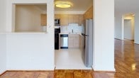 This single-floor residence offers a thoughtfully designed layout that balances open living spaces with practical functionality. Throughout the main living and bedroom areas, richly toned parquet wood flooring adds warmth and classic character, polished to a high sheen that reflects natural light beautifully.

The living area is generously proportioned, featuring clean white walls, a ceiling fan with integrated lighting, and a large window fitted with blinds that brings in ample natural light while offering views of the surrounding neighborhood. A radiator beneath the window provides efficient heating.

The bedroom is well-sized and includes an impressive wall of built-in closets with louvered bi-fold doors, offering exceptional storage capacity. An additional closet with sliding doors further enhances organizational options.

The kitchen has been tastefully updated with light wood cabinetry, white quartz countertops, a subway-style backsplash, and white tile flooring. It is equipped with a full suite of stainless steel appliances, including a gas range, dishwasher, microwave, and refrigerator — combining modern convenience with a clean, contemporary aesthetic.

The bathroom is finished in crisp white, featuring a full bathtub with shower, a toilet, and light tile flooring, creating a bright and functional space. Overall, the residence presents a clean, move-in ready environment with a timeless yet updated appeal.
