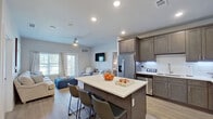 This single-floor residence showcases a thoughtfully designed open-concept layout that seamlessly connects the kitchen, dining, and living areas. The kitchen is a standout feature, equipped with rich dark-toned shaker-style cabinetry, sleek white quartz countertops, a classic white subway tile backsplash with under-cabinet lighting, and stainless steel appliances including a French door refrigerator, dishwasher, and range. A central island with bar seating provides additional prep space and a casual dining option. The adjoining living area is bright and inviting, benefiting from natural light through large windows and a glass door that opens to an outdoor area. A ceiling fan adds comfort, and light wood-look flooring runs consistently throughout the space. The bedrooms are well-sized, each featuring ceiling fans, ample natural light, and the same cohesive wood-look flooring. One bedroom comfortably accommodates twin beds, while another offers a more intimate setting with dedicated dresser space. A vanity area with a white desk connects the private areas of the home. The bathroom presents a clean, all-white design with white shaker cabinets, quartz countertops, tile flooring, and a full tub-shower combination, delivering a crisp and functional finish.