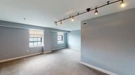 This single-floor residence is thoughtfully designed with a consistent cool-gray color palette that lends a calm, cohesive ambiance throughout. The open living area is a standout feature, showcasing plush wall-to-wall carpeting, crisp white trim, and a sleek track lighting system that provides both task and ambient illumination. Multiple windows dressed with neutral roller shades allow generous natural light to filter in, brightening the generously proportioned space.

The kitchen is outfitted with dark espresso cabinetry, white countertops, and a full suite of stainless steel appliances, including a range, refrigerator, and built-in ventilation. Light wood-look flooring grounds the kitchen, creating a clean contrast to the surrounding cabinetry.

The bedrooms continue the soft gray tones and carpeted flooring, each benefiting from multiple windows that frame exterior views and invite ample daylight. The rooms offer a comfortable sense of scale with clean, uncluttered walls.

Two bathrooms complete the layout. One features a floating vanity with a white integrated sink, a framed mirror, and stylish industrial-style light fixtures. The second bathroom includes a full tub-shower combination with classic white tile surround and wood-look flooring, maintaining the residence's modern yet understated aesthetic throughout.