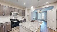 Located at 5220 Center St in Williamsburg, VA, this well-appointed one-bedroom, one-bathroom unit offers a thoughtfully designed single-floor layout. The open-concept kitchen serves as the heart of the home, showcasing rich dark cabinetry, granite countertops, a central island with an undermount sink, pendant lighting, and a full suite of stainless steel appliances including a refrigerator, range, and microwave. The kitchen flows seamlessly into the living area, which features durable hardwood-style flooring, a ceiling fan, and sliding glass doors that open to a private balcony, filling the space with natural light. The bedroom is carpeted for comfort, fitted with a ceiling fan, and includes access to natural light through a dedicated window. Two closets provide ample storage throughout the unit. The bathroom offers a full tub-shower combination. A dedicated laundry area houses a full-size side-by-side washer and dryer, adding everyday convenience. Neutral warm tones, clean white trim, and recessed lighting give the space a modern yet welcoming ambiance throughout.